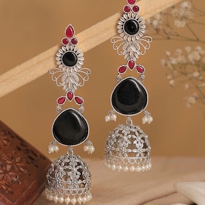 May include: A pair of silver-toned earrings with black and red accents. The earrings feature a floral design with black teardrop-shaped stones and small white pearls. The earrings have a bell-shaped bottom.