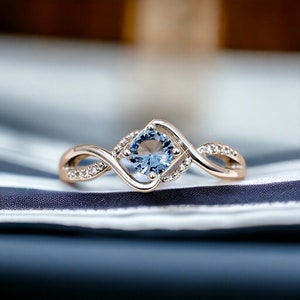May include: A delicate gold ring with a blue gemstone set in a twisted band. The ring is accented with small clear stones.