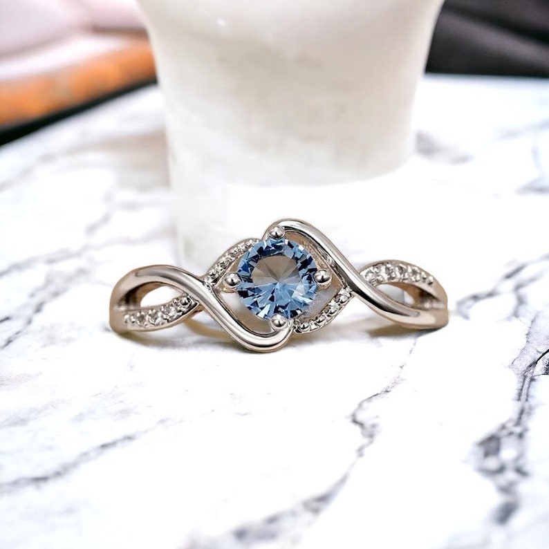 May include: A silver ring with a blue gemstone set in a twisted band. The band is accented with small clear stones.
