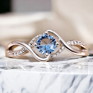 May include: A delicate ring with a blue gemstone set in a twisted band. The band is accented with small clear stones.