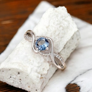 May include: A silver ring with a blue gemstone set in a twisted band. The band is accented with small clear stones.