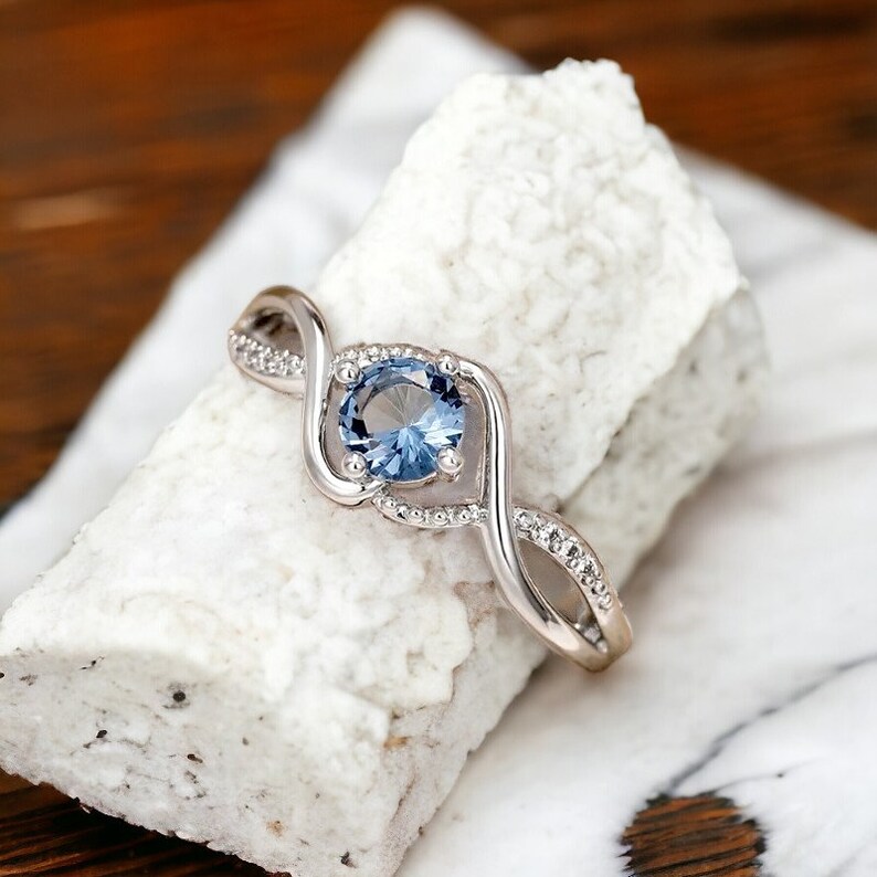 May include: A silver ring with a blue gemstone set in a twisted band. The band is accented with small clear stones.