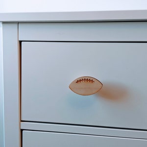 Peut inclure: Commode blanche avec une poignée de tiroir en forme de ballon de football en bois.