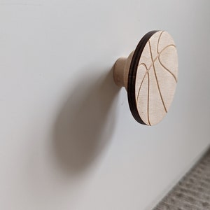 Peut inclure: Un bouton de porte en bois en forme de ballon de basket. Le bouton est brun clair avec une bordure brun foncé et un motif de ballon de basket blanc.