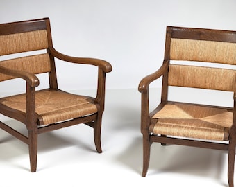 May include: Two wooden armchairs with woven straw seats and backs. The chairs have a dark brown finish and curved armrests. The seats and backs are a light tan color, creating a contrast with the dark wood.