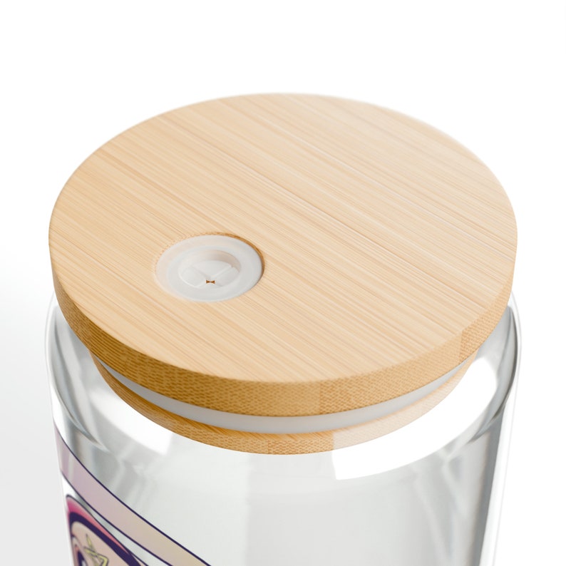 Close-up of a clear glass jar with a light brown bamboo lid. The lid has a small white plastic stopper in the center. The jar is partially visible, showing a white rim and a hint of a colorful design.