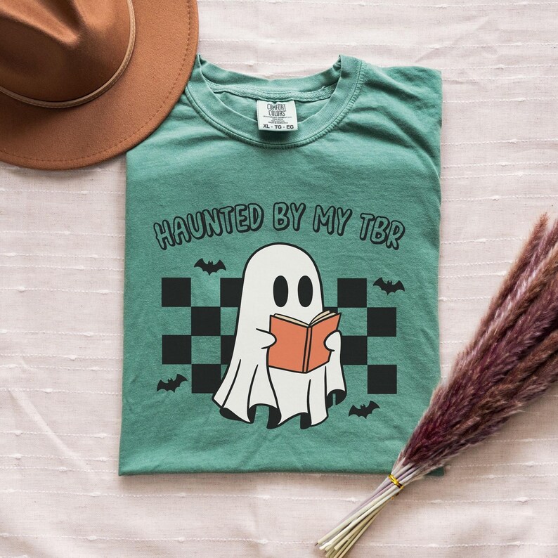 A ghost reading a book, bats and a retro pattern in the background. Text reads haunted by my tbr.