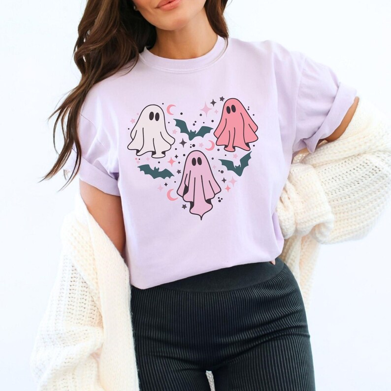 A light purple shirt with a heart-shaped design featuring three ghosts in pink and white with bats and stars.