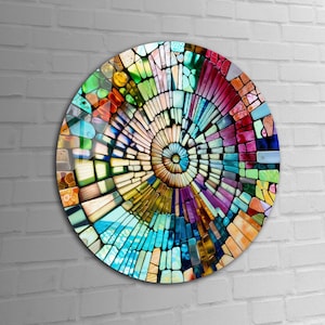 Op de afbeelding: Een cirkelvormig wandkunstwerk met een kleurrijk moza&iuml;ekontwerp. De moza&iuml;ek is gemaakt van kleine, onregelmatige stukjes glas in verschillende tinten blauw, groen, geel, oranje, rood en paars. De stukjes zijn in een spiraalvorm gerangschikt, waardoor een gevoel van beweging en diepte ontstaat.