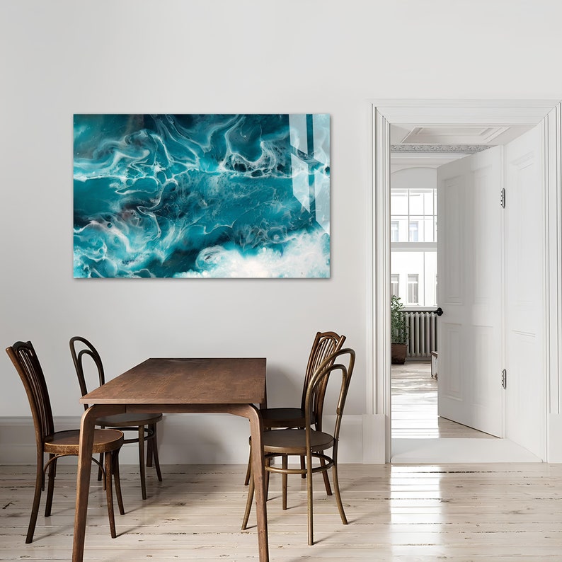 Puede incluir: Impresi&oacute;n de arte abstracto con pintura azul y blanca en espiral, que recuerda a las olas del oc&eacute;ano. La impresi&oacute;n se muestra en una pared blanca sobre una mesa de comedor de madera con cuatro sillas.