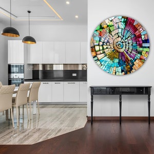 Op de afbeelding: Een kleurrijk rond moza&iuml;ek wandkunstwerk met een spiraalvormig ontwerp. De kunst hangt aan een witte muur in een moderne keuken met een zwart aanrechtblad en witte kasten.