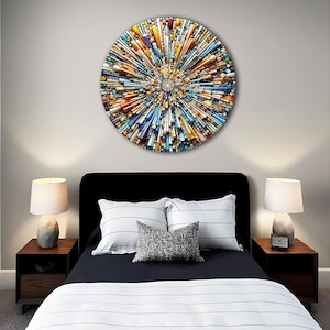 May include: A colorful circular wall art piece with a geometric design. The art is made of various shades of blue, yellow, orange, and white. The art is hanging on a wall above a bed with white and blue striped bedding.