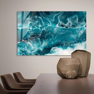 Puede incluir: Impresi&oacute;n de arte abstracto con pintura azul y blanca en espiral, que recuerda a las olas del oc&eacute;ano. La impresi&oacute;n se muestra en una pared sobre una mesa de madera con dos sillas y dos jarrones de vidrio decorativos.