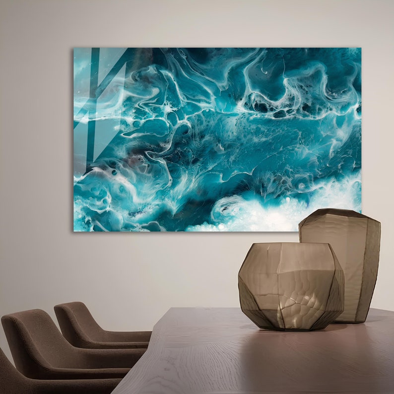 Puede incluir: Impresi&oacute;n de arte abstracto con pintura azul y blanca en espiral, que recuerda a las olas del oc&eacute;ano. La impresi&oacute;n se muestra en una pared sobre una mesa de madera con dos sillas y dos jarrones de vidrio decorativos.