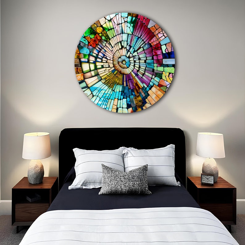 Op de afbeelding: Een kleurrijk cirkelvormig wandkunstwerk met een moza&iuml;ekontwerp. De moza&iuml;ek is gemaakt van kleine, kleurrijke vierkanten en rechthoeken die in een spiraalvorm zijn gerangschikt. Het kunstwerk hangt aan een muur in een slaapkamer.