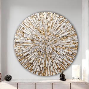 May include: A large, round wall art piece with a mosaic design. The artwork features a radial pattern of white and gold elements, creating a sunburst effect. The piece is mounted on a white wall, and the overall aesthetic is modern and decorative.