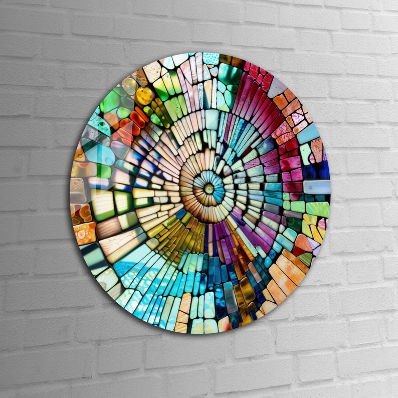 Op de afbeelding: Een cirkelvormig wandkunstwerk met een kleurrijk moza&iuml;ekontwerp. De moza&iuml;ek is gemaakt van kleine, onregelmatige stukjes glas in verschillende tinten blauw, groen, geel, oranje, rood en paars. De stukjes zijn in een spiraalvorm gerangschikt, waardoor een gevoel van beweging en diepte ontstaat.