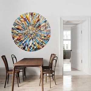 May include: A circular wall art piece with a colorful abstract design. The design features a variety of shapes and colors, including blue, yellow, orange, and white. The art piece is hanging on a white wall in a dining room setting.