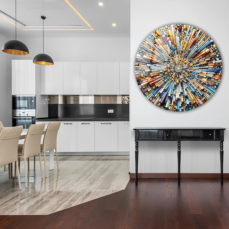 May include: A colorful abstract circular wall art piece with a geometric design. The art is hanging on a white wall above a black console table with three drawers. The table has four legs and is in a modern dining room with a white kitchen in the background.