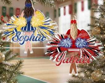 May include: Two flat hanging ornaments featuring illustrations of cheerleaders. One shows a brunette with a blue uniform and yellow pom-poms with the name Sophia. The other shows a blonde with a red uniform and blue pom-poms with the name Gabriel.