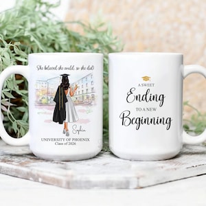 May include: Two white ceramic mugs. One mug features a graduation illustration with the text "She believed she could, so she did!" and "Sophia, University of Phoenix, Class of 2026." The other mug says "A Sweet Ending to a New Beginning."
