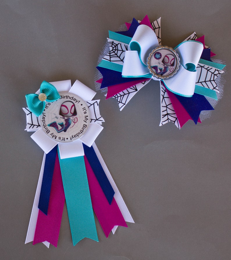 Puede incluir: Dos lazos de cumplea&ntilde;os hechos a mano con tem&aacute;tica de superh&eacute;roes. Uno es una roseta con cintas blancas, turquesas, azul marino y magenta. El otro es un lazo grande con cintas blancas, turquesas, azul marino y magenta, y un dise&ntilde;o de telara&ntilde;a.