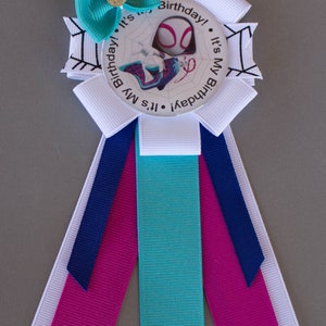 Puede incluir: Una cinta de cumplea&ntilde;os con un dise&ntilde;o de Spider-Gwen. La insignia tiene un lazo turquesa con un centro dorado, cintas blancas y turquesas, y el texto "It's My Birthday!" alrededor de la imagen.