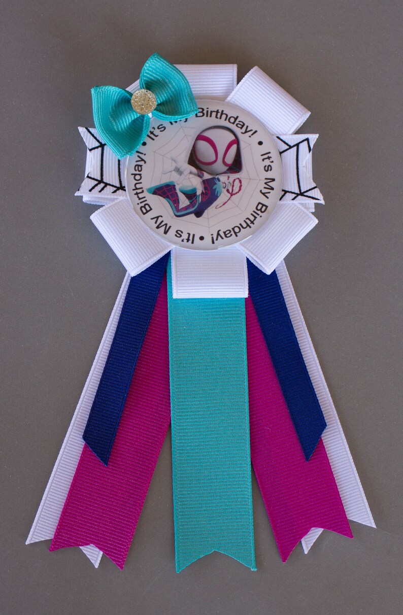 Puede incluir: Una cinta de cumplea&ntilde;os con un dise&ntilde;o de Spider-Gwen. La insignia tiene un lazo turquesa con un centro dorado, cintas blancas y turquesas, y el texto "It's My Birthday!" alrededor de la imagen.