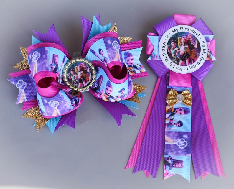 May include: A large, multi-layered hair bow and a matching rosette. The bow features purple, pink, and turquoise ribbons with a character print and gold glitter accents. The rosette has a "It's My Birthday!" message.