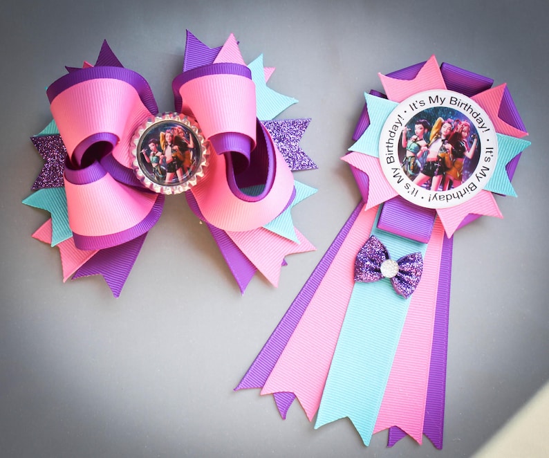 May include: Two handmade birthday accessories. One is a large pink, purple, and teal bow with a photo in the center. The other is a badge with a photo, ribbons, and a small bow. Both have the text "It's My Birthday!"