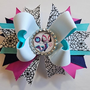 Puede incluir: Un lazo para el cabello hecho a mano con una cinta azul claro con bordes turquesa, superpuesto con cintas rosas, azul marino y turquesa. El lazo tiene un adorno central con un dise&ntilde;o de Spider-Gwen y est&aacute; acentuado con cinta de telara&ntilde;a en blanco y negro.