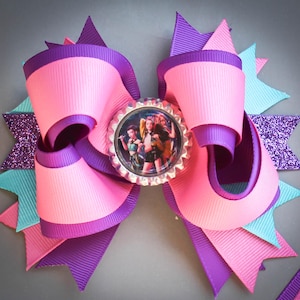 May include: A large, multi-layered hair bow in shades of pink, purple, and turquoise. The bow features a central image within a bottle cap, surrounded by ribbon loops and glitter accents. The bow is designed with a layered effect, creating a visually appealing accessory.