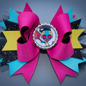 May include: A pink, blue, black, and yellow bow with a glitter accent and a round button featuring a cartoon character with sunglasses. The button is silver with a black border.
