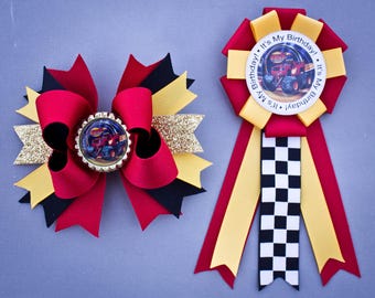 May include: Red, black, and gold bow with a monster truck image in the center. A red, yellow, and black checkered ribbon with the text "It's My Birthday!" in a circle.