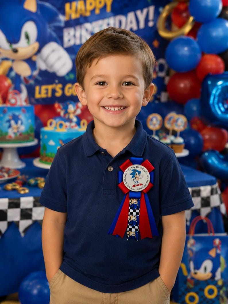 K&ouml;nnte beinhalten: Ein l&auml;chelnder Junge in einem marineblauen Poloshirt und khakifarbener Hose. Er tr&auml;gt eine Geburtstagsrosette mit Sonic the Hedgehog. Der Hintergrund zeigt Sonic-Dekorationen, Luftballons und eine Geburtstagstorte, was eine festliche Atmosph&auml;re schafft.