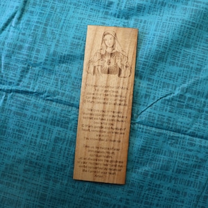 May include: Wooden bookmark with a laser-engraved image of the Virgin Mary and a prayer to the Immaculate Heart of Mary. The prayer reads: "O Immaculate Heart of Mary, full of grace, how we love you!  Our hearts are drawn to your Immaculate Heart, where we find all solace, all help, all peace. We love you as never before, we have a soft heart so that we have a contrite heart, a hungry soul and the thirst of a heart, pure and holy.  Heart, remember us when we are in need. Amen."