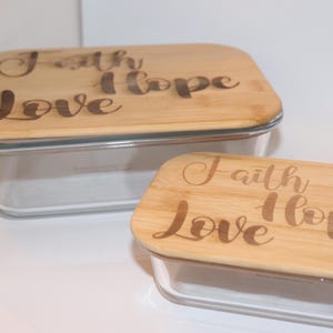 Może przedstawiać: Dwa szklane pojemniki do przechowywania z drewnianymi pokrywkami. Pokrywki są grawerowane słowami "Wiara, Nadzieja, Miłość".