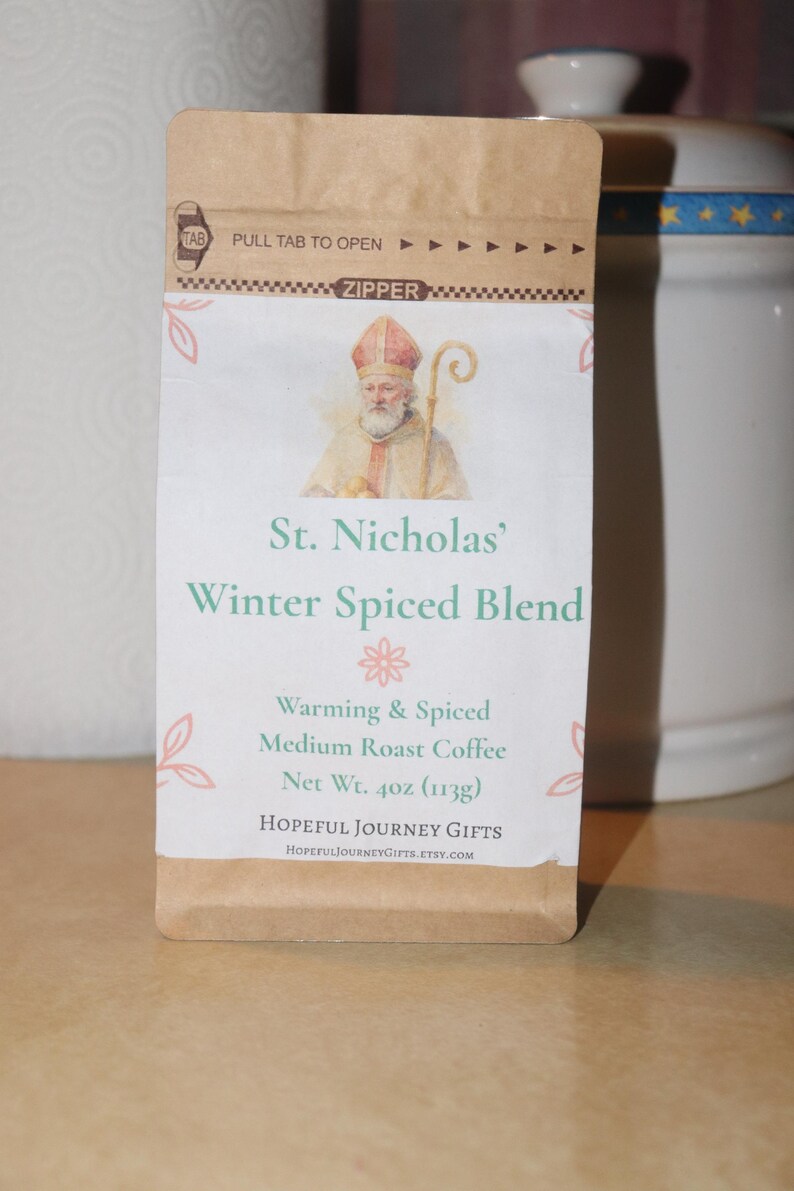 May include: A brown paper bag of St. Nicholas' Winter Spiced Blend medium roast coffee. The bag features an illustration of St. Nicholas and text that reads "Warming & Spiced". Net weight is 4 oz.
