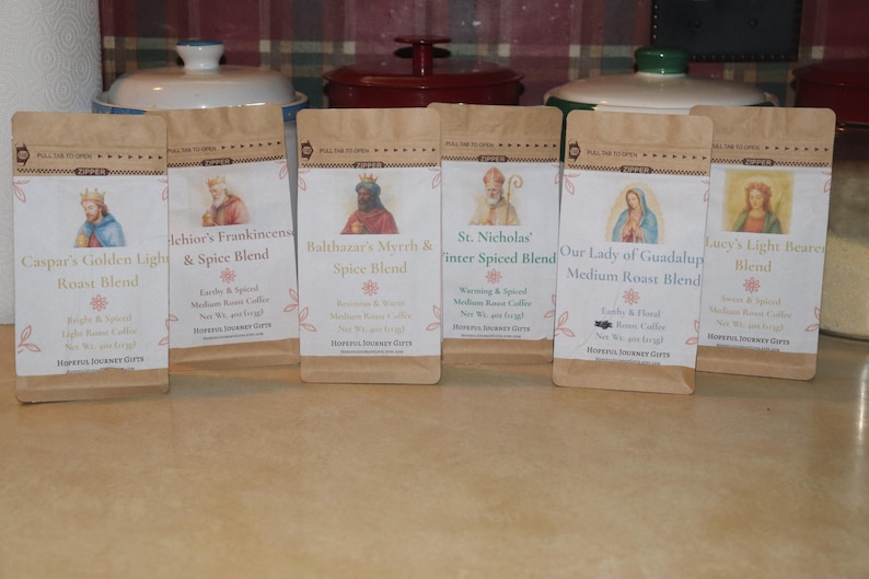May include: Six coffee bags with various blends, including "Caspar's Golden Light Roast Blend" and "St. Nicholas Inter Spiced Blend." Each bag features a different religious figure illustration and text. The bags are brown with white labels and floral accents.