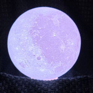 May include: A white moon lamp with a textured surface, glowing with a soft purple light.