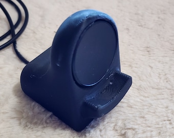 May include: A black 3D printed charging stand for a smartwatch. The stand has a circular indentation for the watch face and a small ledge for the watch band.