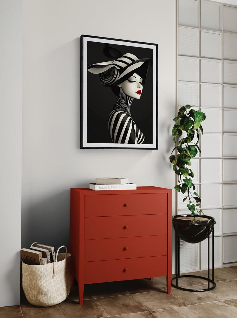May include: A framed wall art print featuring a stylized portrait of a person wearing a black and white striped hat and matching high-neck garment, accented with bright red lips, displayed above a solid red four-drawer chest of drawers.