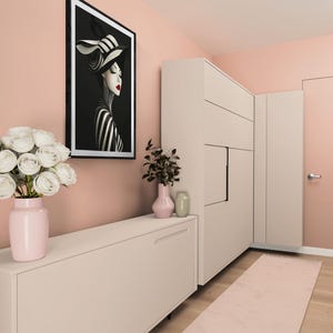 May include: A framed wall art print featuring a stylized portrait of a person in a black and white striped hat and outfit with red lips, displayed in a room with a light pink cabinet, a pink vase with white roses, and a tall beige storage unit.