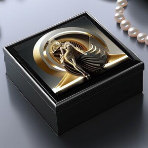 May include: A black square jewelry box with a gold and silver design on the lid. The design features a stylized figure in a gold dress and a geometric pattern.