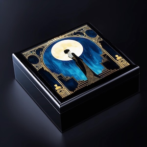 May include: A black wooden box with a gold trim and a blue and gold illustration of a woman standing in front of a large moon. The illustration is on the top of the box.