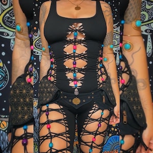 Op de afbeelding: Zwarte bodysuit met uitsnijdingen en vetersluitingen. De bodysuit is versierd met kleurrijke kralen en heeft een zwarte riem met een geometrisch ontwerp.