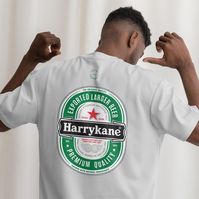 May include: A white short-sleeved t-shirt featuring a large graphic on the back. The design is a green, white, and red oval beer label style logo with the text "Harrykane" in a black banner, "Exported Larger Beer," and "Premium Quality."