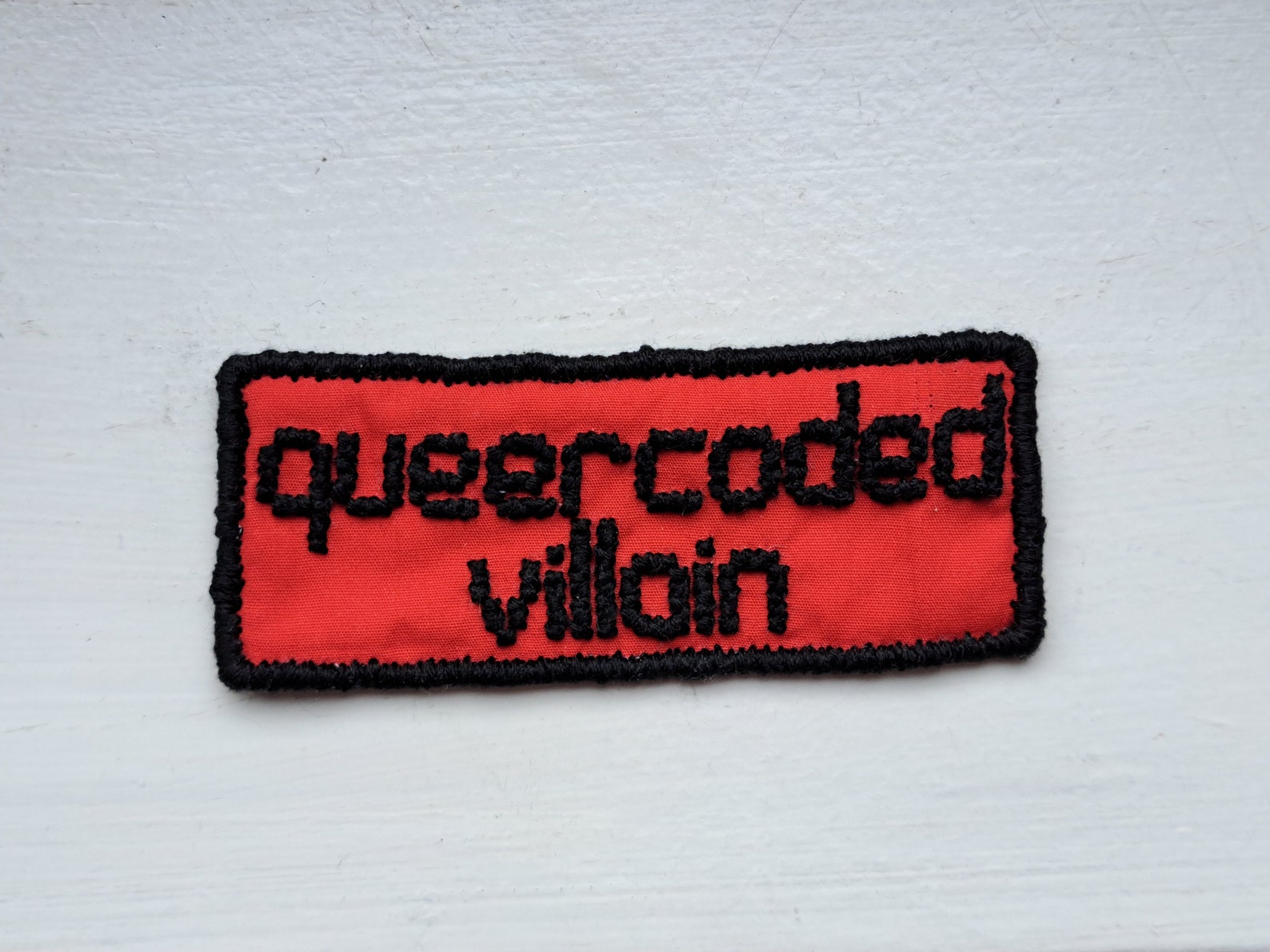 Queercoded Villain cross-stitched patch in black and red