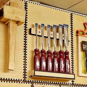 Puede incluir: Un juego de siete cinceles para tallar madera con mangos rojos y viroles metálicas azules están montados en un soporte de pared de madera. Los cinceles están dispuestos en orden de tamaño, con el cincel más grande a la izquierda y el más pequeño a la derecha. Todos los cinceles están afilados y listos para usar.