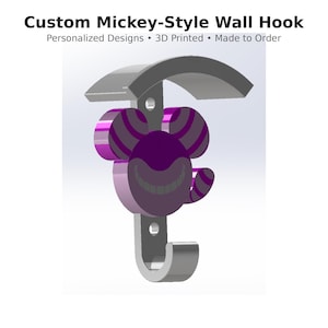 May include: A custom Mickey-style wall hook with a unique design. The hook features a purple and gray Cheshire Cat face and ears, with a curved top and a hook at the bottom. The text reads: "Custom Mickey-Style Wall Hook".